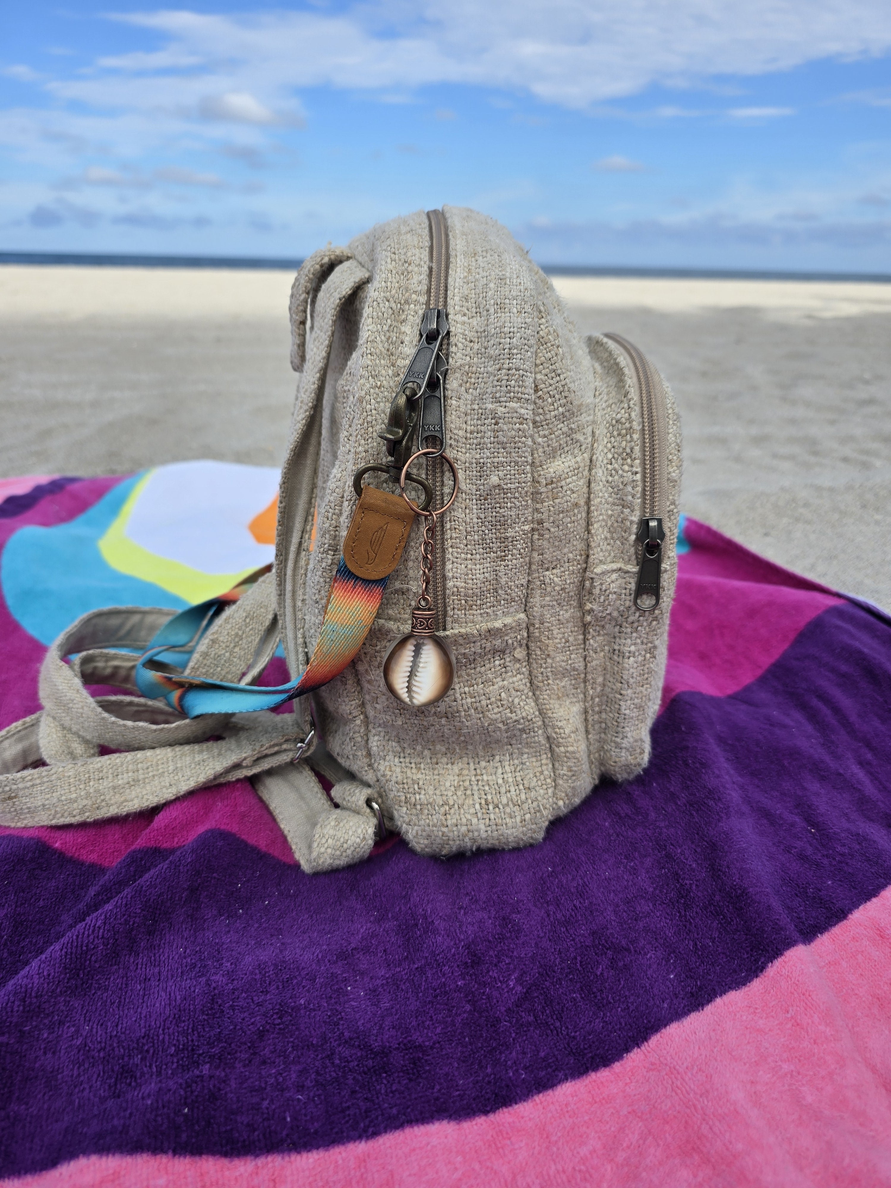Brown cowrie shell resin orb keychain clipped to a beach backpack