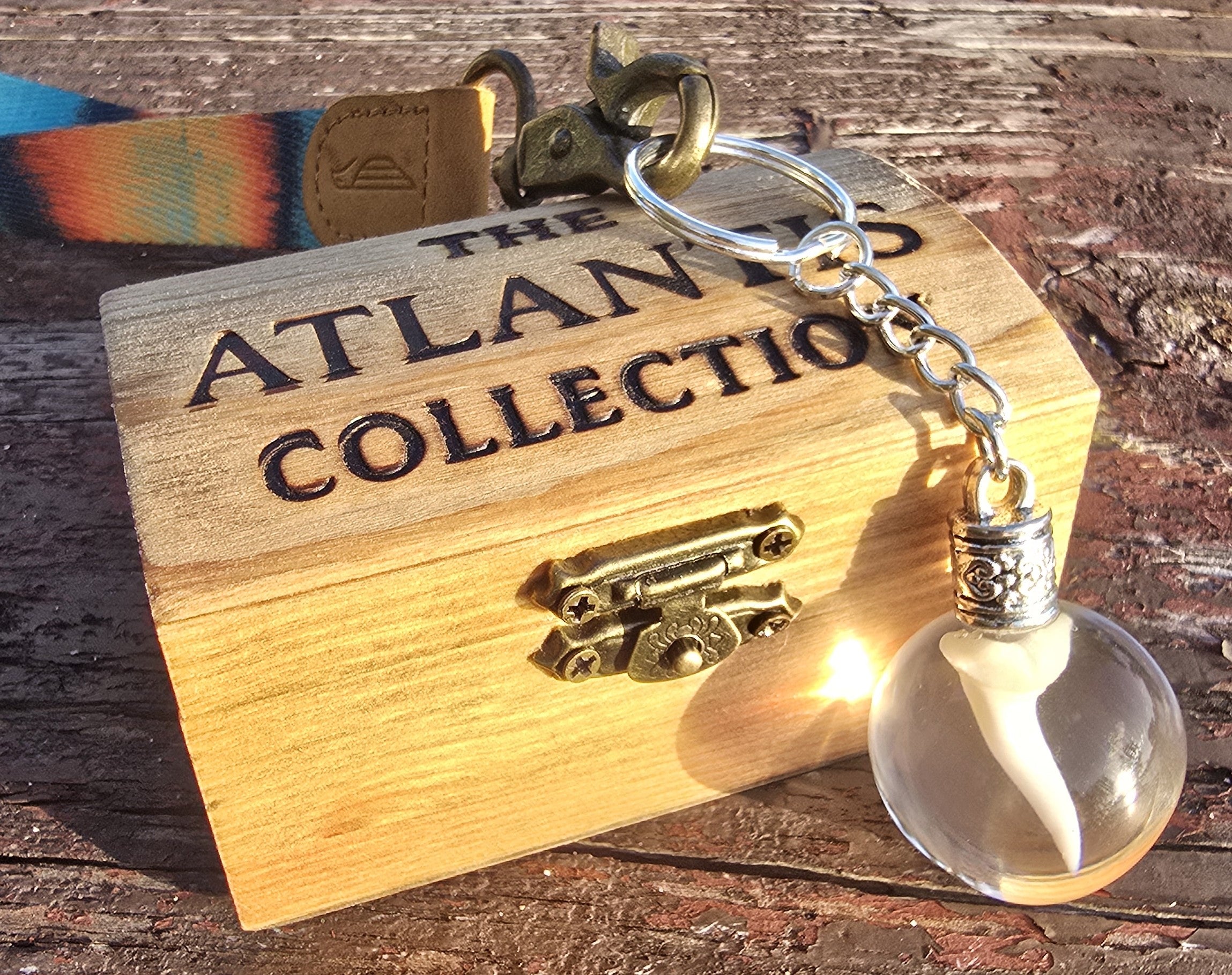 Mako shark tooth resin keychain resting on an engraved Atlantis Collection wooden box on rustic wood