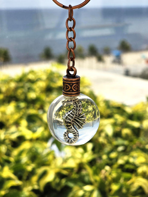Silver seahorse charm suspended in a clear resin orb keychain with an ocean backdrop
