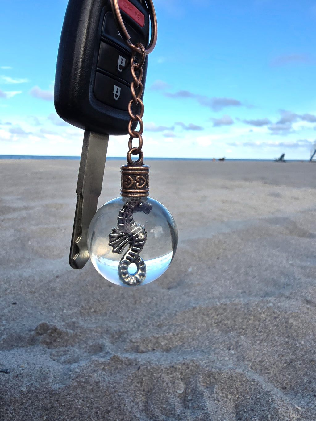 Seahorse of Atlantis resin orb keychain clipped to a car key on the beach
