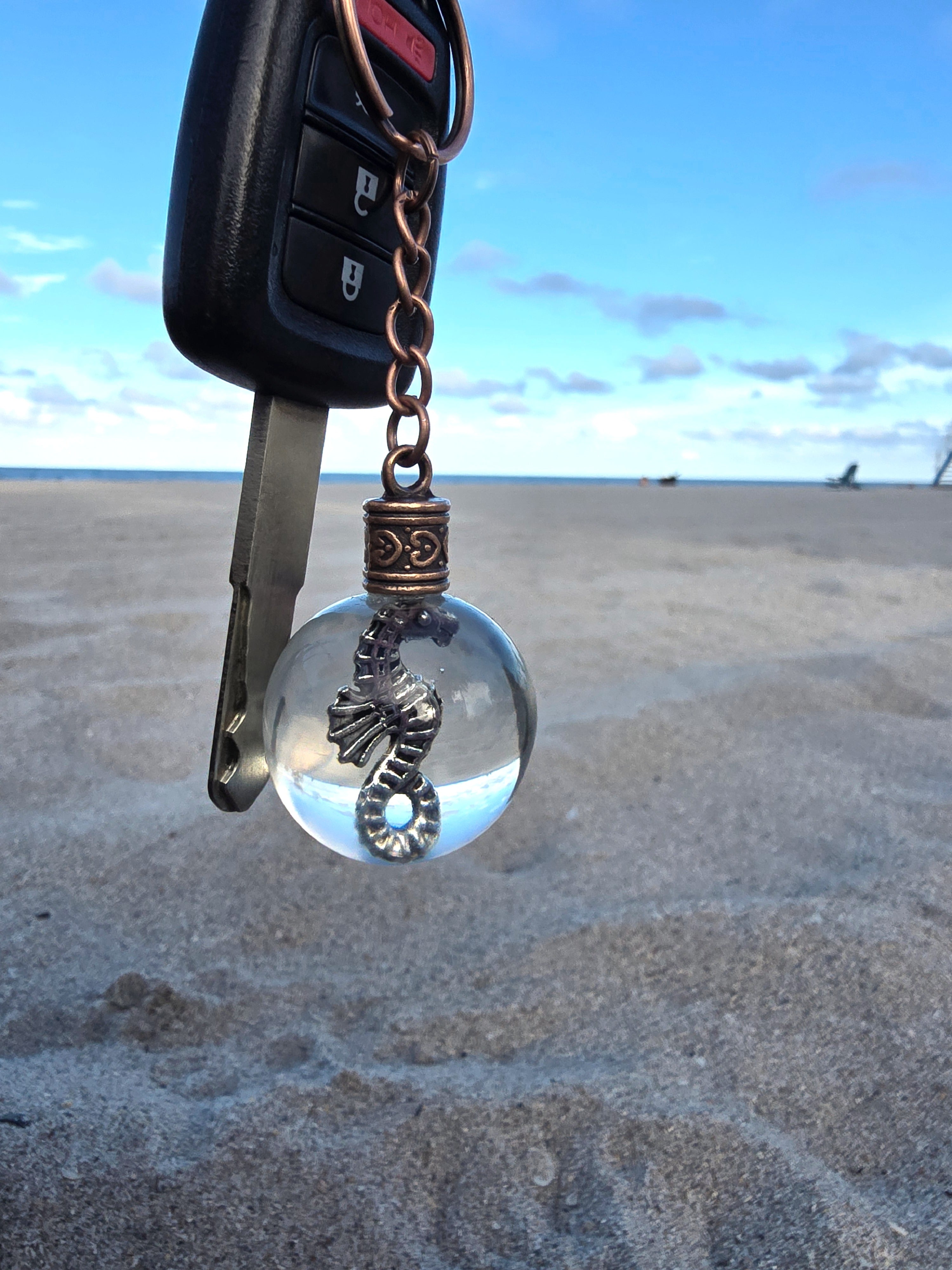 Seahorse of Atlantis resin orb keychain clipped to a car key on the beach