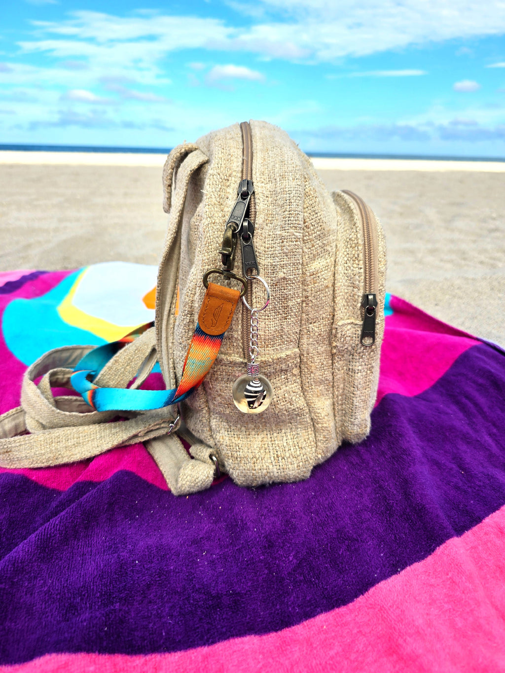 Zebra Cone Shell resin orb keychain clipped to a beach backpack